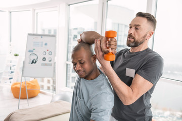 Exercise with dumbbells. Smart young man lifting weights while exercising with his therapist