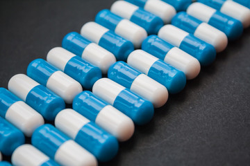blue and white pills or capsules lies in a rows on black background close up