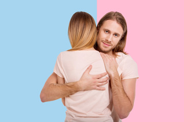 Love wins. Pleasant loving man giving his girlfriend a tender hug while standing between blue and...