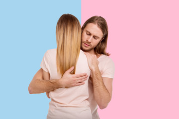 Never let go. Handsome young man holding his girlfriend in a tight embrace and closing his eyes in a surge of feelings while standing between pink and blue backgrounds