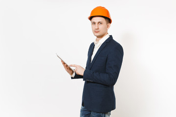 Young handsome successful businessman in dark suit, protective construction helmet holding tablet pc computer isolated on white background. Male worker for advertisement. Business, working concept.