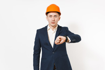 Shocked businessman in dark suit, protective construction orange helmet looking on clock on hand isolated on white background. Time is running out. Male worker for advertisement. Business concept.