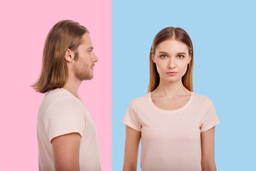 Always you. Well-built young man with longish hair standing sideways and looking at his girlfriend while she standing against a blue background and staring at the camera