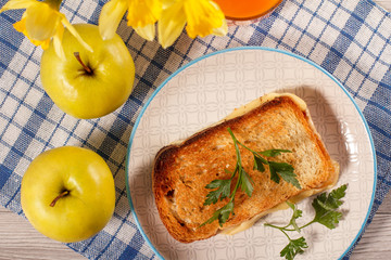 Toast with butter and cheese on white plate, two apples, glass of orange juice and bouquet of spring flowers