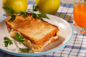 Toast with butter and cheese on white plate, two apples and glass of orange juice.
