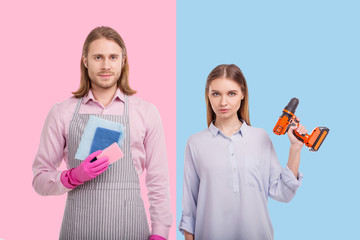 Deconstructing gender stereotypes. Pleasant young man wearing an apron and holding sponges while...