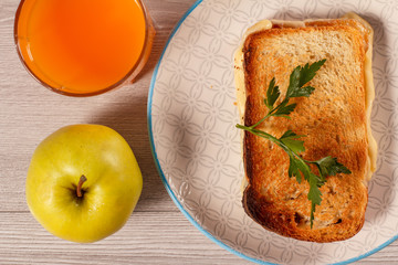 Toast with butter and cheese on white plate, apple and glass of orange juice.