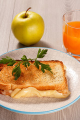 Toast with butter and cheese on white plate, apple and glass of orange juice.