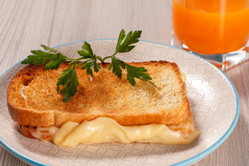 Toast with butter and cheese on white plate and glass of orange juice.