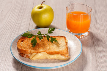 Toast with butter and cheese on white plate, apple and glass of orange juice.