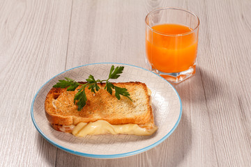 Toast with butter and cheese on white plate and glass of orange juice.