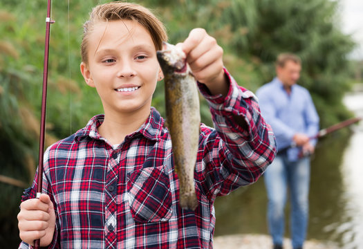 Relaxed teenage boy holding catch freshwater fish