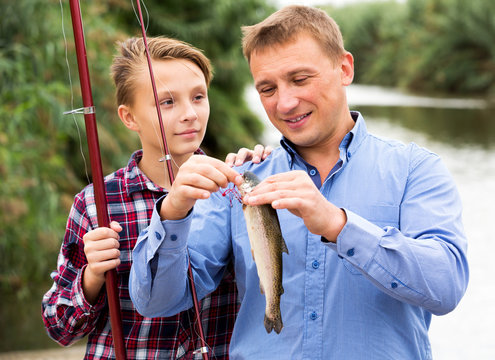 Man with teenager boy releasing fish from hook