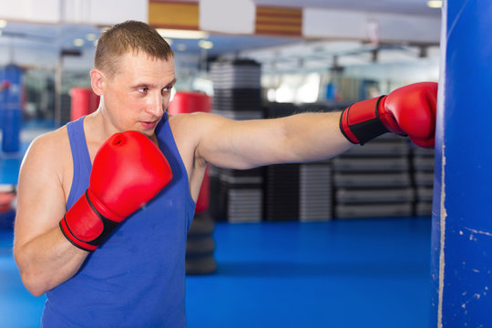 Man is training with punching bag in box gym