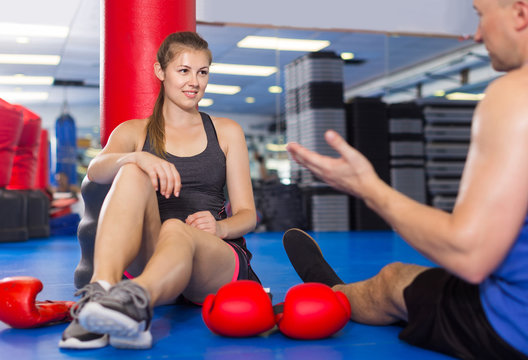 Female boxer is sitting with man and talking about healthy in gym.