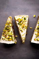 Raw vegan pistachio carrot cake with cashew cream layers from above on concrete table. Dark food photography styling concept. Vertical