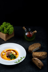 An appetizing pumpkin soup is served in a white plate in a restaurant