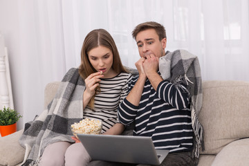 I am terrified. Frightened young man watching a film with his girlfriend eating popcorn