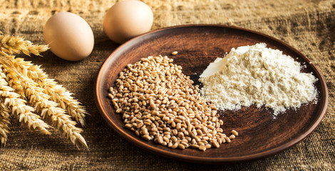 wheat flour eggs and spikelets of wheat on sackcloth background