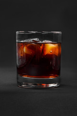 A single-colored transparent cocktail, refreshing in a low glass with radiant ice cubes with a taste of berries, cherries, strawberries, grapefruit, cola. Side view Isolated black background