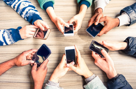 Hands circle using phones on table top view - Multiracial group of people holding mobile devices sitting around at office desk - Concept  of modern technology addiction