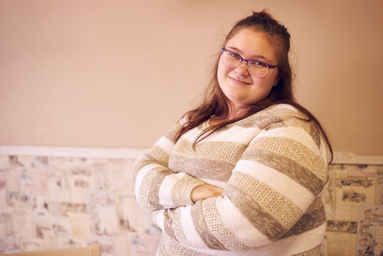Portrait of beautiful chubby caucasian woman standing in front of a two toned wall with decorated wall paper and her arms crossed while looking at camera and smiling.