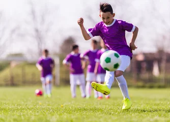 Rolgordijnen Boy kicking football on the sports field © Dusan Kostic