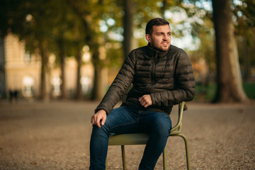 Obraz premium Handsome man sits in the middle of the park in khaki stool