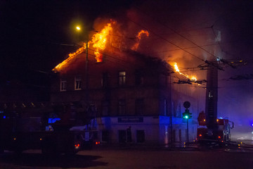 Firemen direct water stream on burning house.building in full flaming inferno, and a firefighter fighting to get control of the flames.