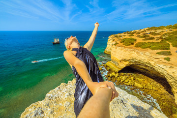 Follow me, woman holding hand at Algarve coast famous for rock formations. Benagil sea cave on the...