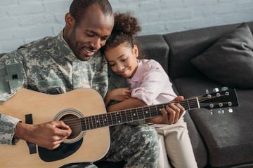  Smiling soldier playing guitar and hugging daughter