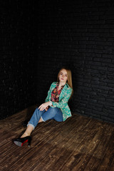 Naklejka premium Stylish blonde girl in jacket and jeans against brick black wall at studio.