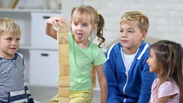 Four children of primary school age putting wooden blocks on top of each other when trying to make toy tower as tall as possible