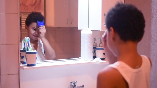 Cute African American boy combs his curly hair in the bathroom by the mirror. Children and hygiene. How to care for children.