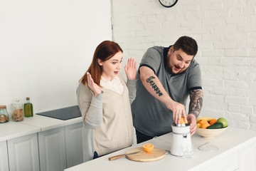 surprised size plus girlfriend looking how boyfriend preparing orange juice at home