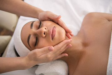 Fototapeta na wymiar Facial procedure. Attractive nice woman lying with her eyes closed while enjoying facial massage