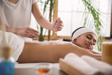 Obraz na płótnie Canvas Salty massage. Professional female masseuse holding salt while putting it on her clients back