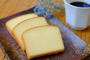 Homemade plain butter cake soft and moist. Slice of butter cake on plate and serve with black coffee on wood table
