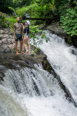 couple standing on Gitgit Waterfall with green plants on background, Bali, Indonesia