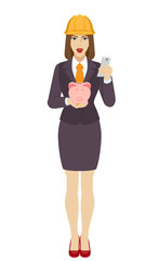 Businesswoman in construction helmet using a mobile phone and holding a piggy bank