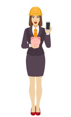 Businesswoman in construction helmet holding a piggy bank and mobile phone
