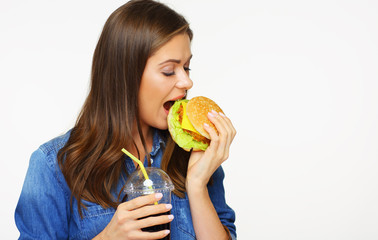 Woman with closed eyes biting burger holding cola drink in glass