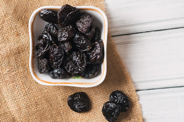 Prunes in ceramic plate on wooden background