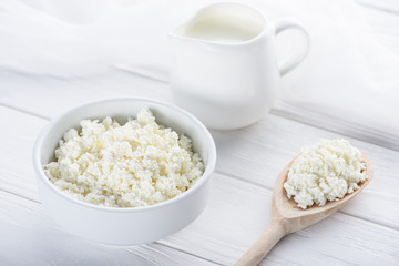 close-up view of fresh healthy cottage cheese, wooden spoon and milk in jug on wooden table