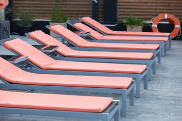 Fototapeta na wymiar orange chaise lounges stand in a row on the beach or near the pool, in the background a life ring, no people