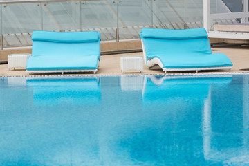 Two wide turquoise deck chairs are beside the pool, reflected in the water, concept travel, vacation