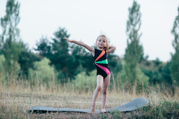 Little cute girl gymnast sits on a splits on mats in the woods