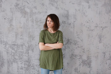 Disappointed sad woman folded her arms on chest looking somewhere away on the gray wall background. Copyspace