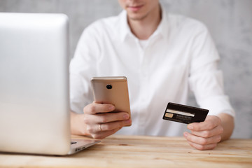 Hands of young blurry unidentified man holding bank card and smartphone while shopping in an online store
