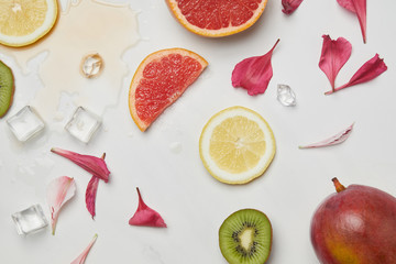 top view of arrangement of fresh exotic fruits, ice cubes and flower petals on white surface